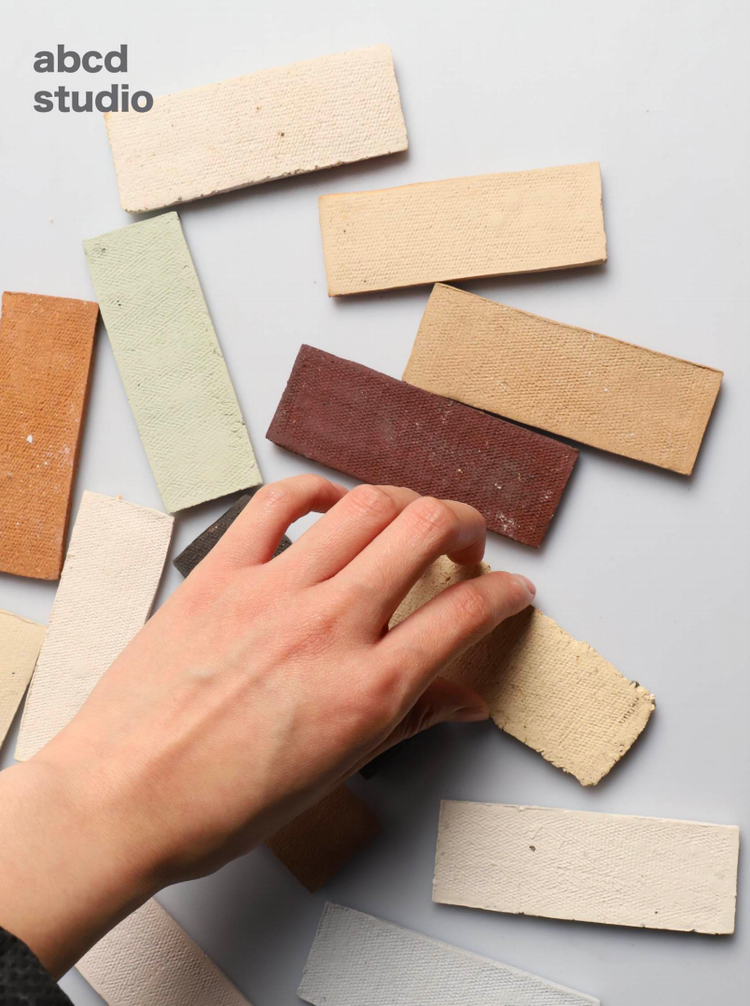 Hand touching a row of raw clay color and texture swatches at abcd studio