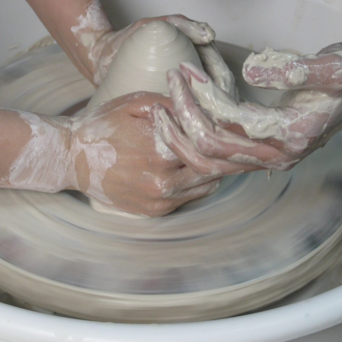 Close-up of an artist's hands shaping wet clay on a pottery wheel