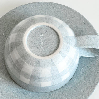 Bottom view of grey gingham ceramic cup on matching saucer, showing Twoto maker's signature